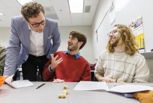 Professor leaning over students playing a game at a classroom table